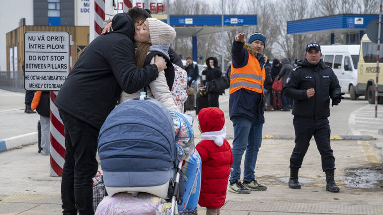 Eine Frau mit Kinderwagen und Kleinkind verabschiedet sich an der Grenze von ihrem Mann