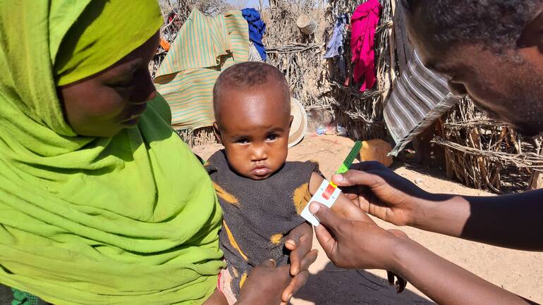 Die kleine Suldana auf dem Arm ihrer Mutter: Ein Mitarbeiter von Aktion gegen den Hunger untersucht sie mit einem MUAC-Band auf Mangelernährung.