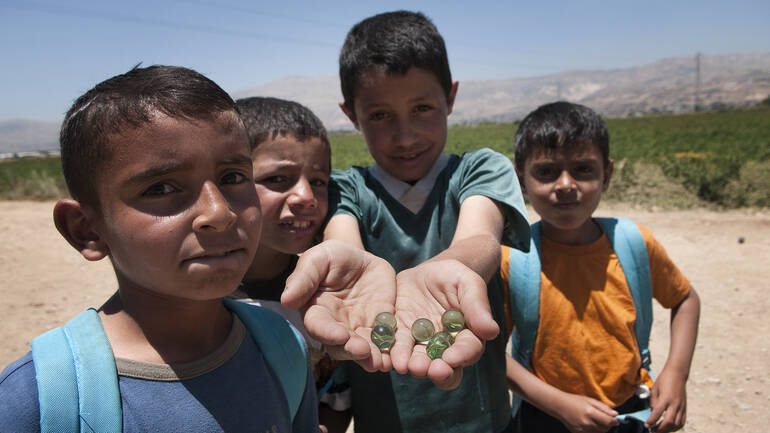 Vier Jungs aus dem Libanon schauen in die Kamera, einer zeigt Murmeln auf seiner Hand.