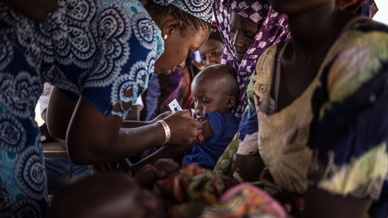 Eine Frau aus dem Senegal untersucht ein Baby auf Mangelernährung.