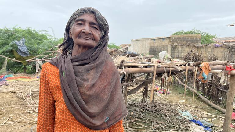 Eine ältere Frau steht vor ihrem zerstörten Haus