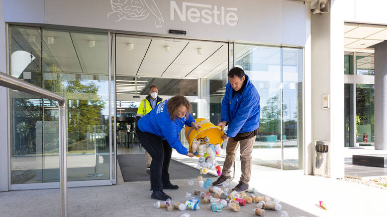 Zwei Mitarbeitende von Aktion gegen den Hunger schütten eine gelbe Wanne voller Babymilch-Flaschen vor dem Eingang der Nestlé-Zentrale in Frankfurt aus.