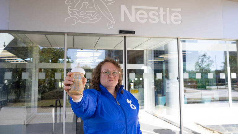 Eine Mitarbeiterin von Aktion gegen den Hunger in blauer Jacke steht vor den Türen der Nestlé-Zentrale in Frankfurt und hält eine Flasche mit dreckiger Babymilch in die Kamera