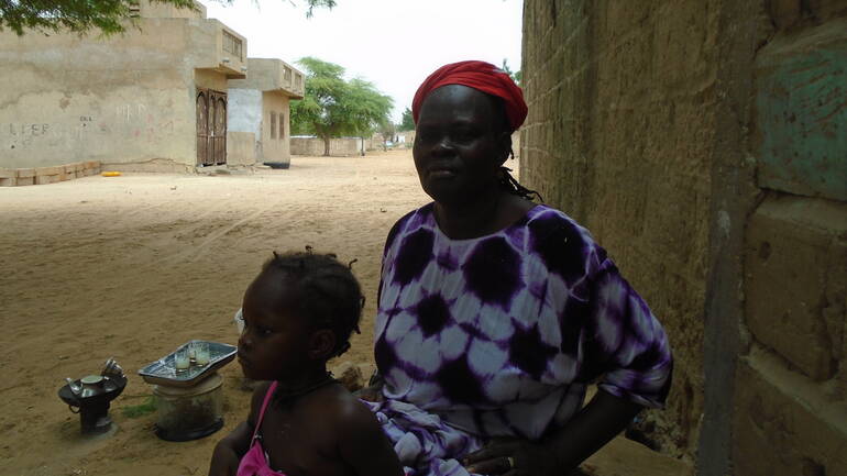 Großmutter Tening steht zusammen mit einer Enkelin an einer Kochstelle im trockenen Dorf