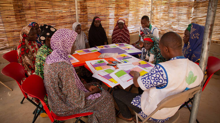 Frauen aus Burkina Faso mit zwei Gesundheitsmitarbeitern bei einer Gruppentherapie-Sitzung, auf dem Tisch liegen Arbeitsblätter