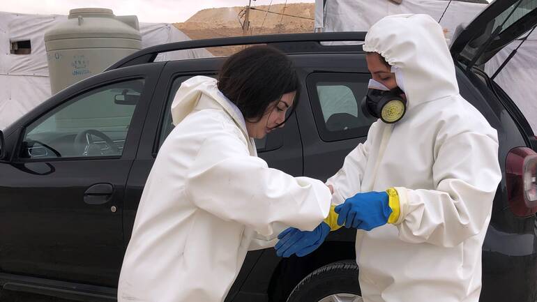 Zwei Mitarbeiterinnen helfen sich gegenseitig beim Anziehen von Schutzkleidung, um sich vor Cholera zu schützen.