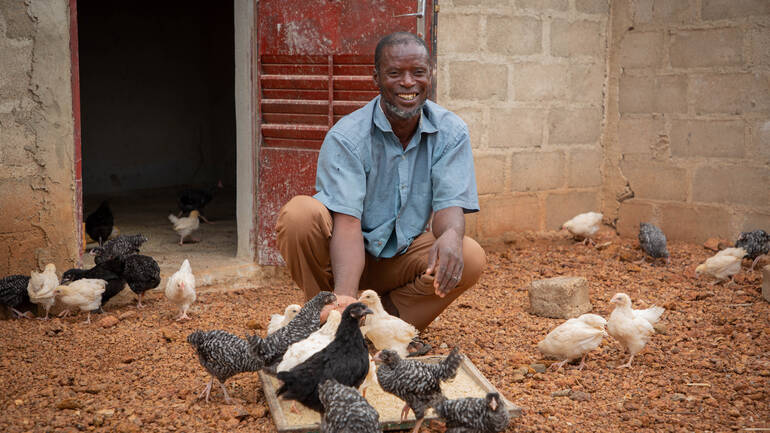 Ein Mann aus Burkina Faso posiert bei seinen Hühnern im Gehege.