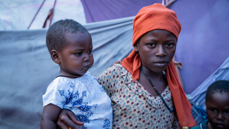 Junge Frau mit Kind auf dem Arm in einem Geflüchteten-Camp in Mogadishu, Somalia.