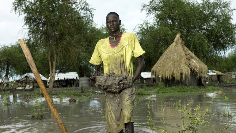 Nach verheerenden Überschwemmungen im Südsudan baut ein junger Mann einen Damm aus Schlamm, um sein Haus zu schützen.