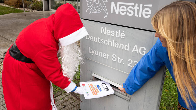 Der Nikolaus wirft mithilfe einer Campaignerin die Petitionsunterschriften in den Briefkasten der Nestlé-Zentrale in Frankfurt am Main.