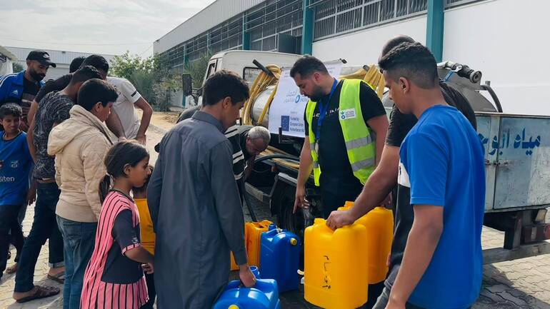 Ein Mitarbeiter von Aktion gegen den Hunger vor einem Wassertruck verteilt Kanister mit frischem Wasser an Kinder und Jugendliche in Gaza.
