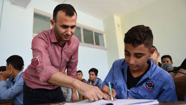Hilal Kabi ist Lehrer und zeigt einem seiner Schüler etwas in einem Heft.