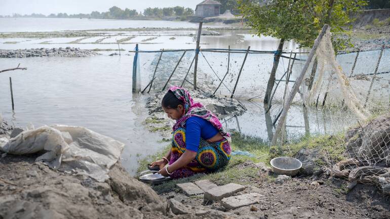 Eine Frau aus Bangladesch kniet am Wasser