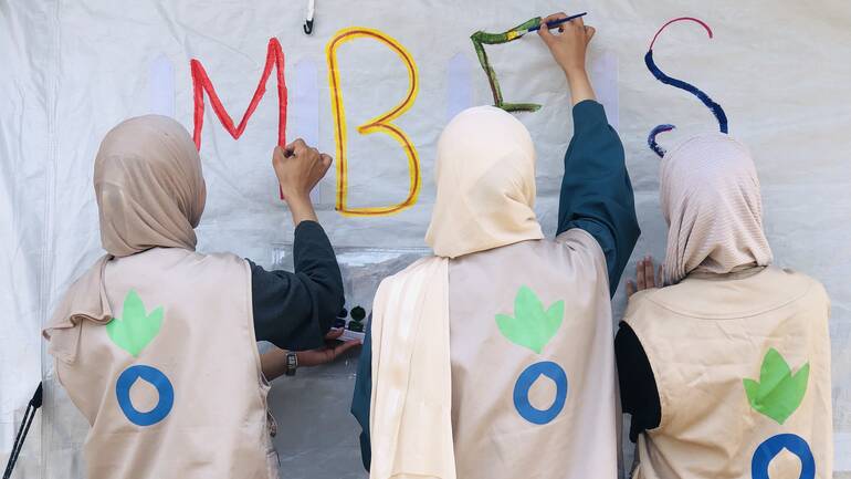 Mitarbeiterinnen von Aktion gegen den Hunger bemalen das Zelt mit den Buchstaben MBFS für Mother Baby Friendly Spaces. Mitarbeiterinnen von Aktion gegen den Hunger bemalen das Zelt mit den Buchstaben MBFS für Mother Baby Friendly Spaces.