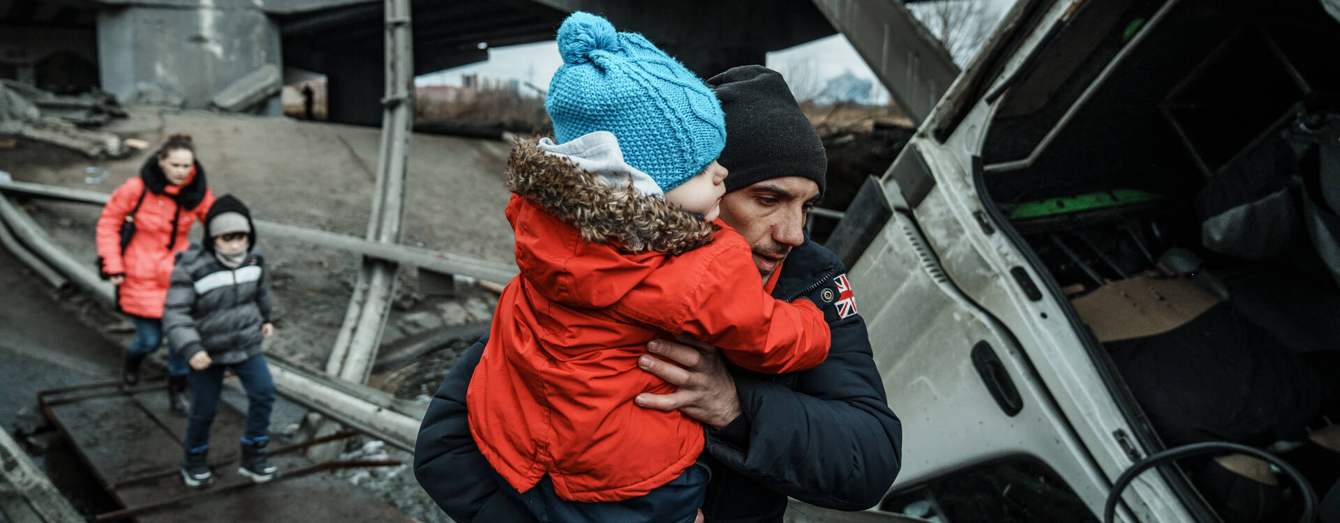 Krieg Ukraine: Mann mit Kind auf dem Arm inmitten von Zerstörung. 