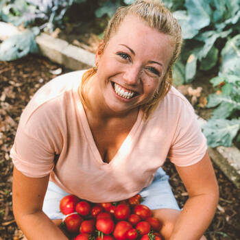 Zora Klipp grinst sitzend in die Kamera im Bauerngarten im Kliemannsland, im Schoß frische Tomaten