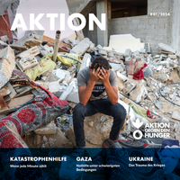 Titelbild AKTION #01/2024 ein junger Mann sitzt in Gaza in den Trümmern eines Hauses und vergräbt das Gesicht in den Händen.
