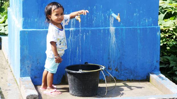 Kind in Indonesien lässt Wasser in einen Eimer ein.