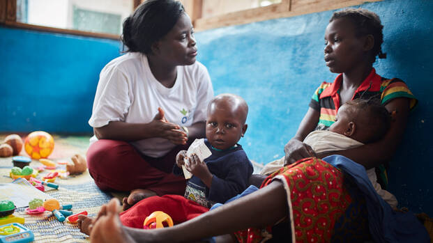 Helferin von Aktion gegen den Hunger hört Mutter mit ihren Kindern zu.