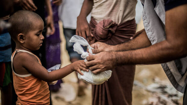 Ein kleiner Rohingya-Junge erhält einen Beutel mit Nahrung.
