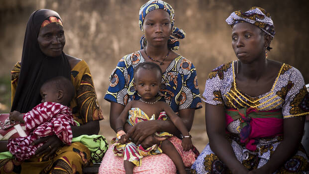 Frauen in Mali sitzen zusammen mit ihren Kindern auf dem Schoß.