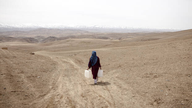 Eine Frau trägt Wasserkanister durch die weite, karge Landschaft Zentralafghanistans
