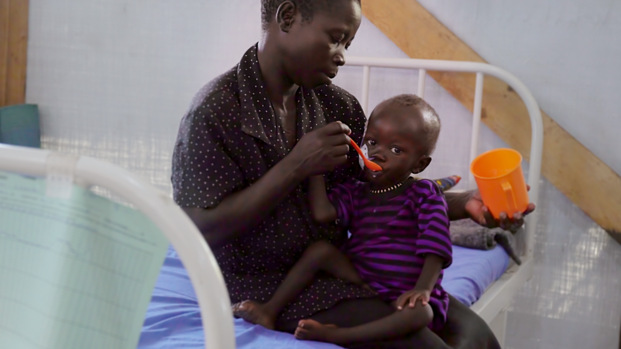 Mutter füttert mangelernährtes Kind in einer Gesundheitsstation von Aktion gegen den Hunger.
