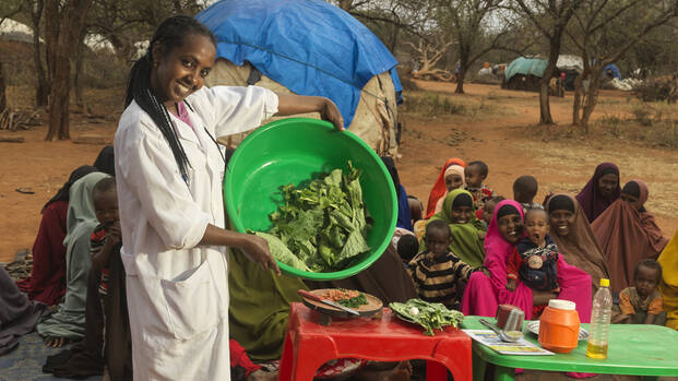 Gelaye Bekele ist Ernährungsspezialistin in Äthiopien und zeigt Familien das Kochen mit frischen Lebensmitteln; hier mit einer Schüssel Salat, im Hintergrund viele lachende Mütter mit Kindern