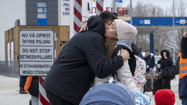 Ein Mann und eine weinende Frau mit Kinderwagen und Kleinkind umarmen sich an der moldawischen Grenze.