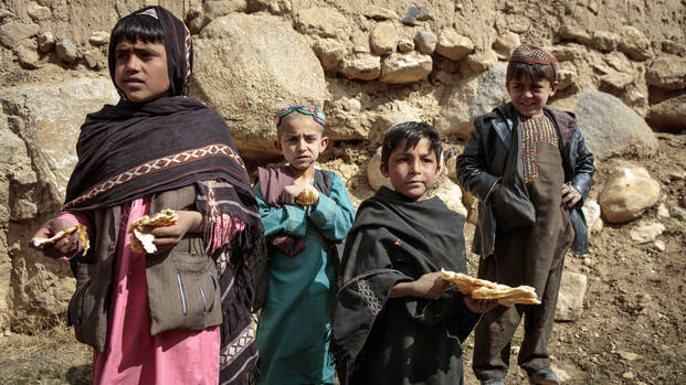 Vier Kinder aus Afghanistan stehen mit Brot in der Hand auf Steinen.