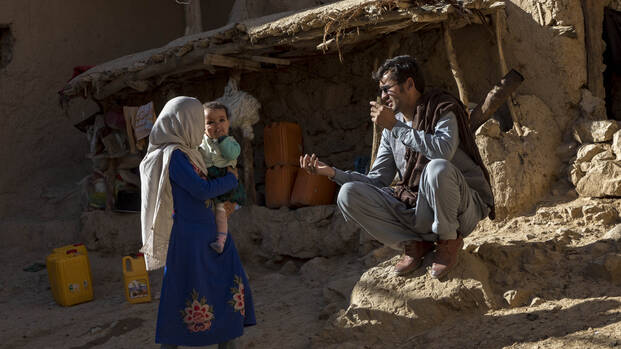 Eine dreiköpfige Familie vor ihrem halb zusammenfallenden Lehm-Haus in Afghanistan