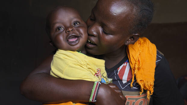 Eine Mutter aus Kenia drückt ihr lachendes Kind liebevoll an sich