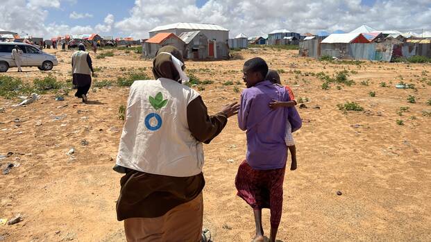 Eine Mitarbeiterin von Aktion gegen den Hunger in Somalia begleitet einen Vater mit Kind auf dem Arm durch ein Camp.