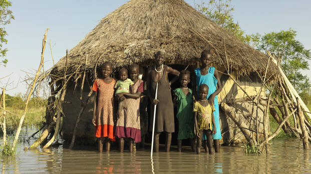 Nyabiele aus dem Südsudan steht mit ihrer Familie vor einer überfluteten Hütte im Dorf