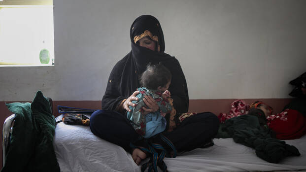 Eine Mutter sitzt mit ihren mangelernährten Zwillingen auf einem Bett in einem unserer Krankenhäuser in Afghanistan.