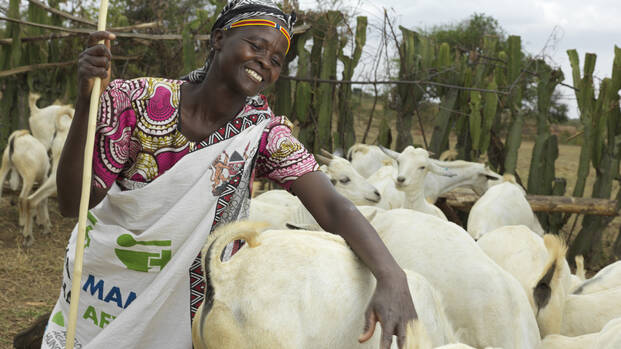 Rosalyne steht lachend im Ziegengehege in Kenia und streichelt eine Ziege.