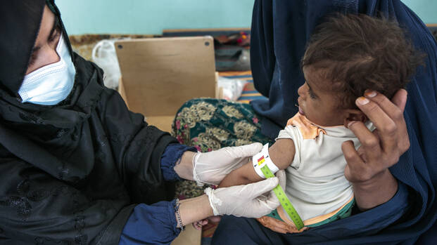 Eine Gesundheitsmitarbeiterin von Aktion gegen den Hunger misst einem Kind in den Armen der Mutter mit einem MUAC-Band den Armumfang.