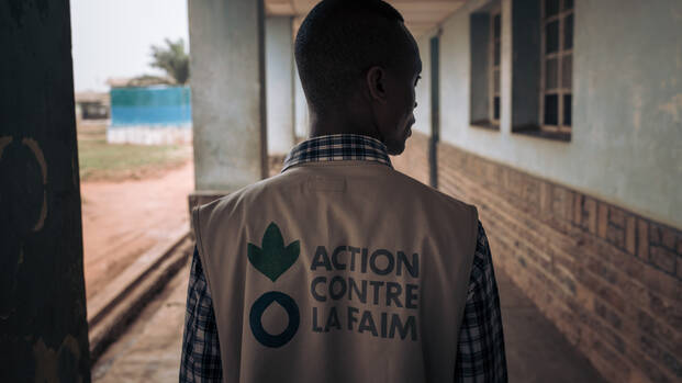 Ein Mitarbeiter von Aktion gegen den Hunger von hinten in einem Gang in der Demokratischen Republik Kongo, auf seiner Weste das Logo