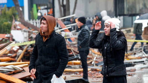 Ein junger Mann und eine junge Frau stehen verzweifelt vor den Trümmern in einer Straße nach dem schweren Erdbeben in der Türkei