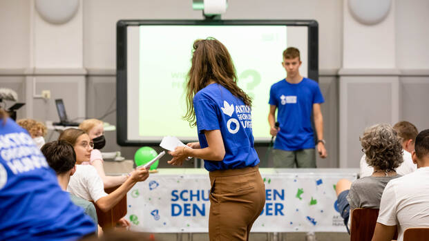 Ein Bildungsvortrag von Schulen gegen den Hunger: Mitarbeiter*innen verteilen Materialien und zeigen eine interaktive Präsentation.