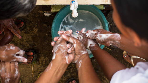 Menschen waschen sich an einem Behelfswaschbecken die Hände mit Seife.