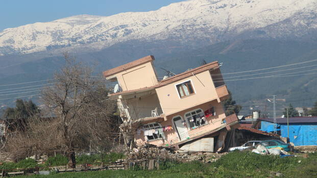 Ein Haus ist nach dem Erdbeben in der Region Hatay zur Seite gekippt, im Hintergrund Berge.