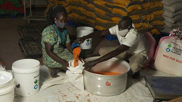 Ein Mitarbeiter von Aktion gegen den Hunger füllt Getreide in einen Sack einer Frau aus dem Südsudan.
