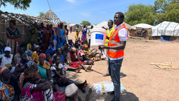 Ein Mitarbeiter von Aktion gegen den Hunger spricht zu Frauen, die im Schatten vor ihm sitzen und aus dem Sudan zurück in den Südsudan geflohen sind.