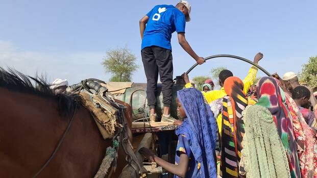 Ein Mitarbeiter von Aktion gegen den Hunger versorgt Geflüchtete aus dem Sudan mit Trinkwasser.