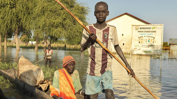 Ein Junge fÃ¤hrt mit einer Ã¤lteren Frau in einem Baumstamm-Boot durch ein Ã¼berflutetes Gebiet im SÃ¼dsudan.