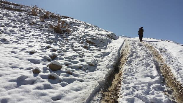 Ein Vater trägt sein Kind über einen verschneiten Weg im winterlichen Afghanistan zu einem abgelegenen Krankenhaus. Die beiden sind nur von hinten zu sehen.