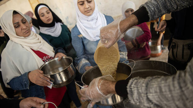 Frauen in einem Shelter in Aleppo erhalten warmes Essen, das in ihre mitgebrachten Töpfe gegossen wird. November 2023