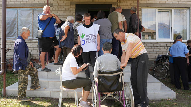 Mitarbeitende von Aktion gegen den Hunger unterstützen ältere Menschen in der Ukraine vor einem Haus.