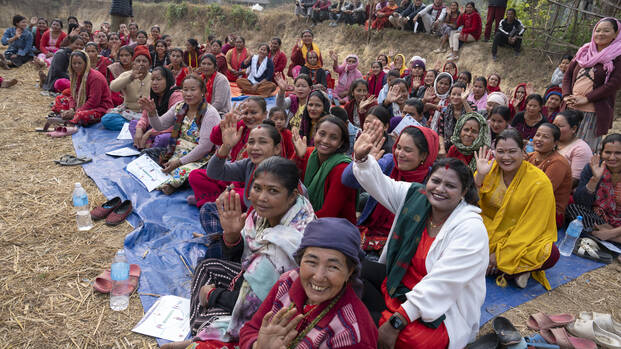 Goma und die anderen Frauen aus ihrem Dorf in Nepal sitzen nach einer Demonstration für Ernährungssicherheit gemeinsam auf dem Boden und winken in die Kamera.